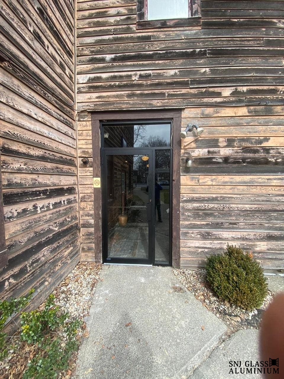 Black-framed glass entry door set into a wood-clad exterior.