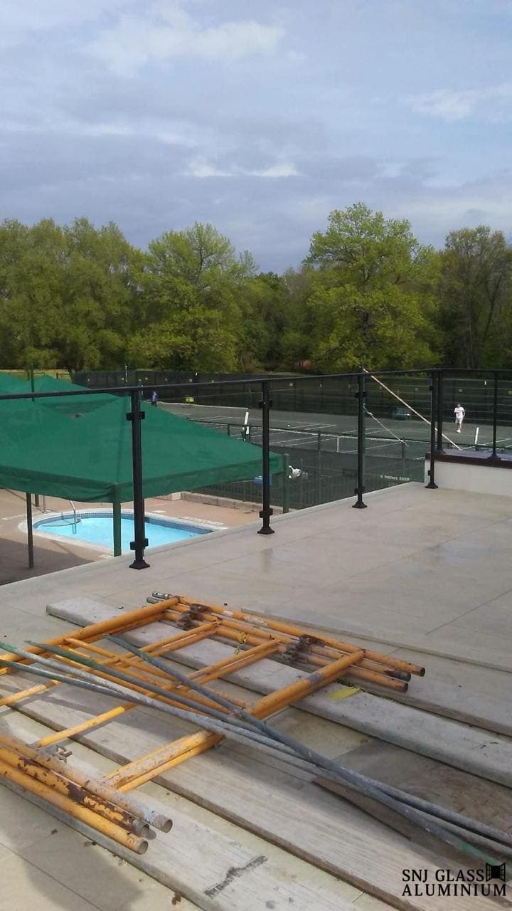 Glass railing with dark posts overlooking outdoor courts and a pool.