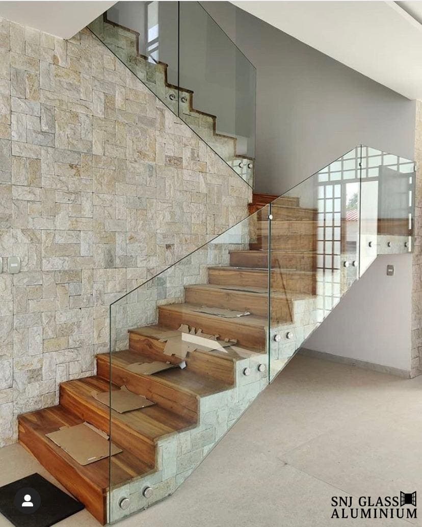 Clear glass railing beside a stone wall and wood staircase.