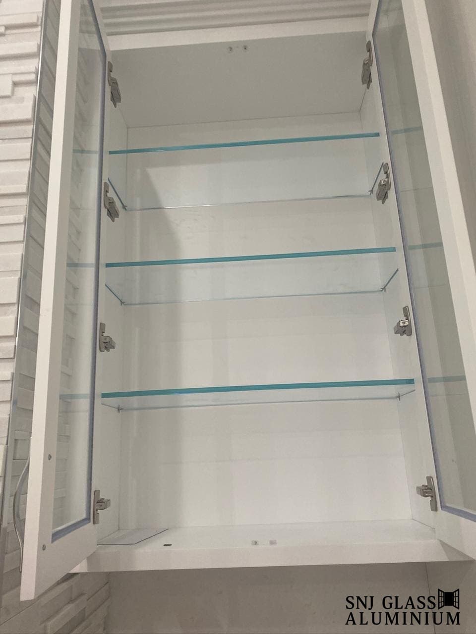 Three glass shelves inside open white cabinetry.