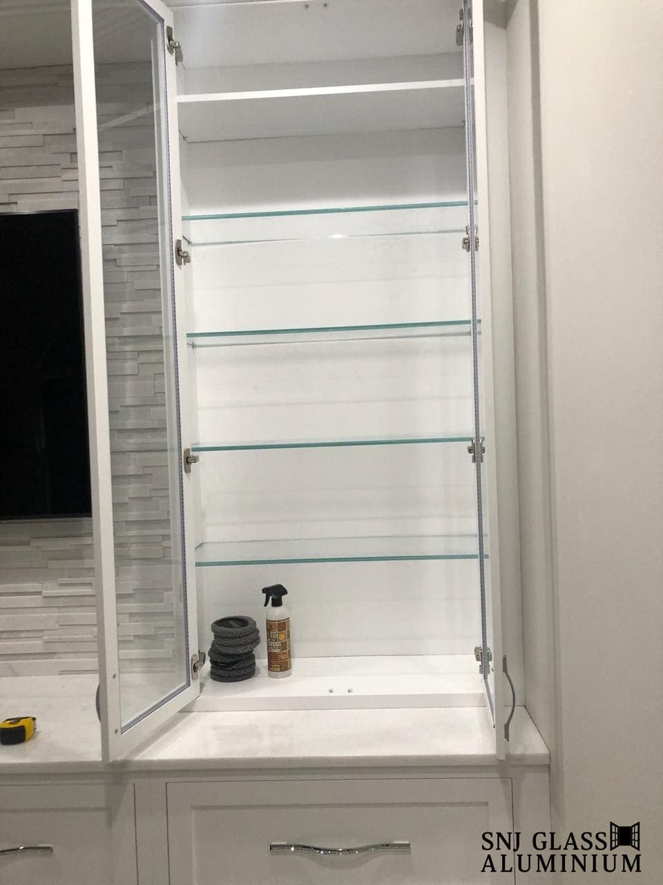 Four glass shelves inside tall open white cabinetry.