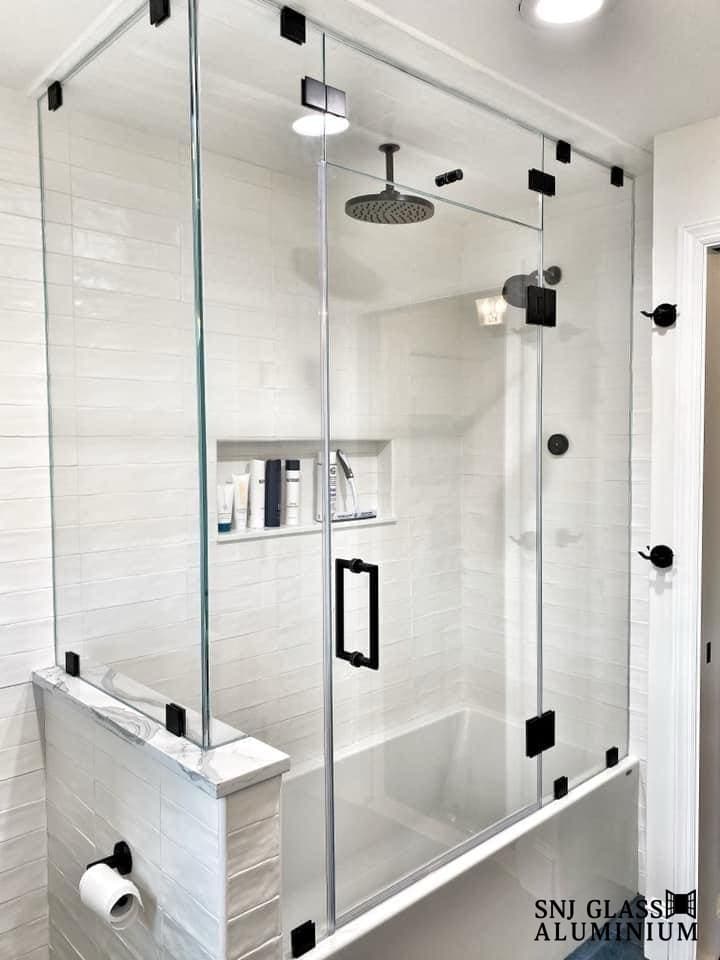 Clear hinged shower door and fixed panel with black hardware.
