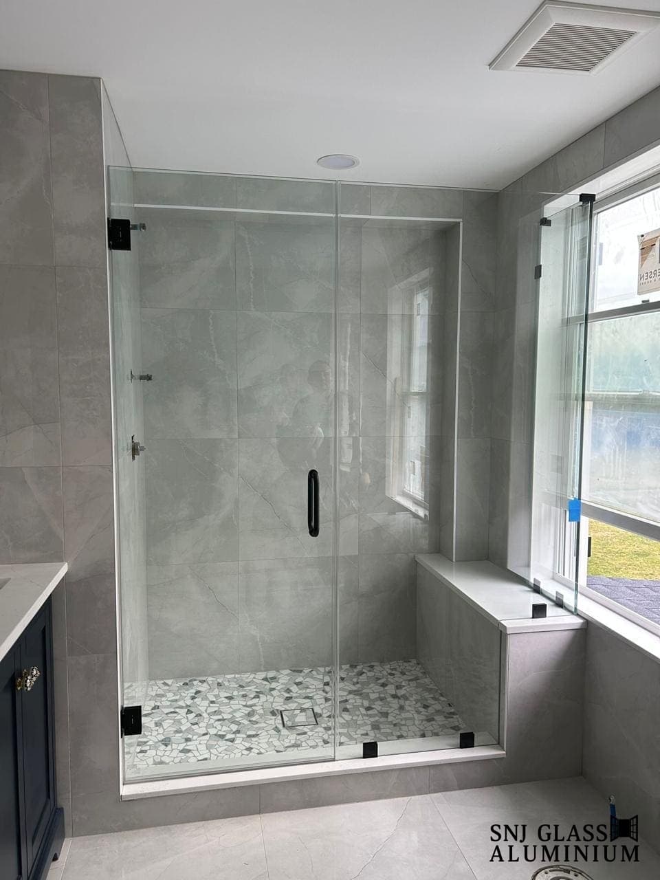Clear hinged shower door and fixed panel in a white-tiled bathroom.