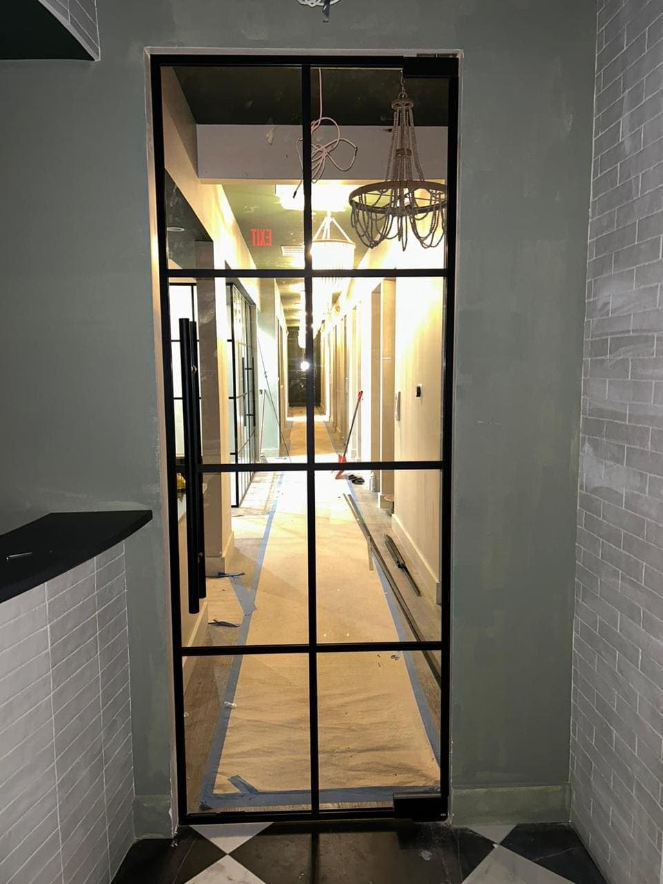 Black grid-framed interior glass door with a long pull handle in a tiled entry under construction.