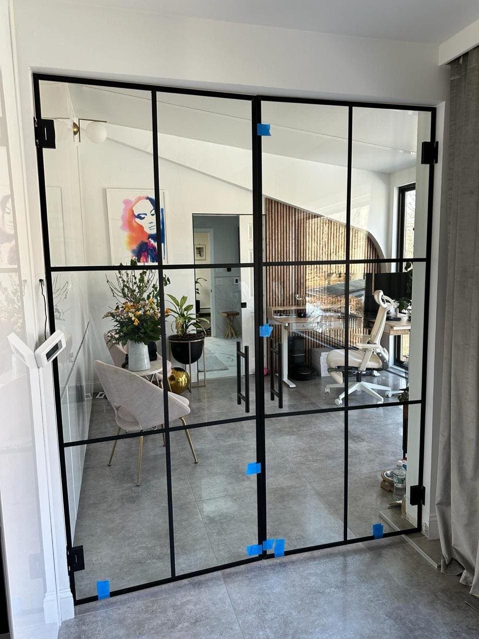 Black grid-framed interior glass partition with blue construction tape visible on the panels.