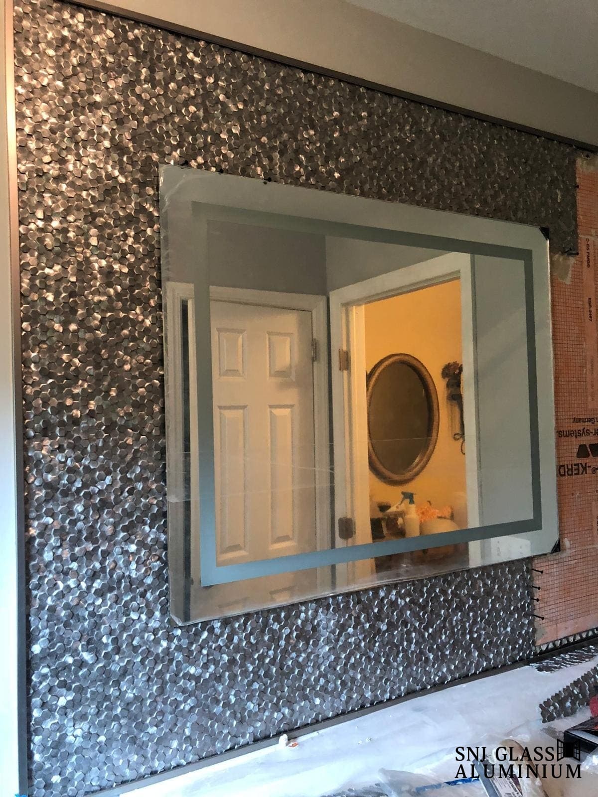 Large rectangular mirror mounted on a mosaic-tiled wall.