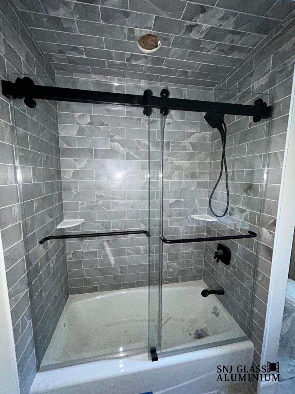 Two-panel sliding tub enclosure with a black rail and towel bars.