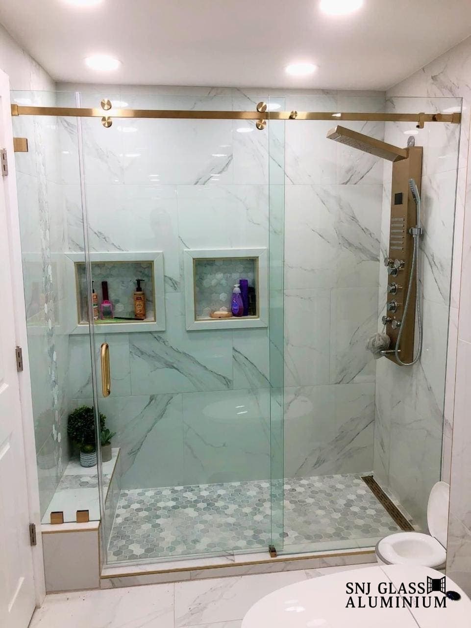Clear sliding shower enclosure with a gold-tone rail and handle.