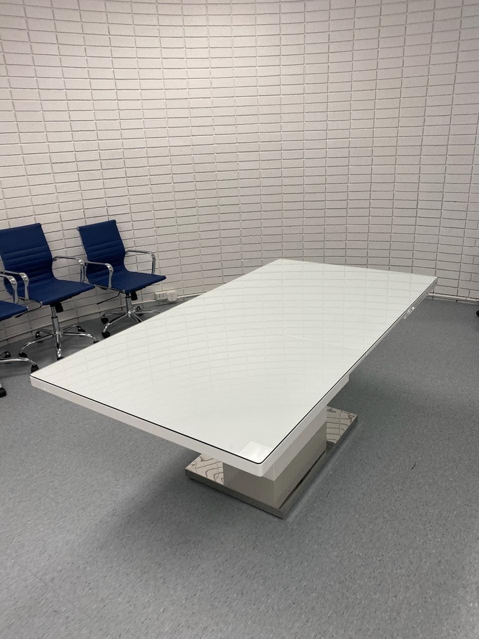 Large rectangular glass top on a white conference table surrounded by blue chairs.