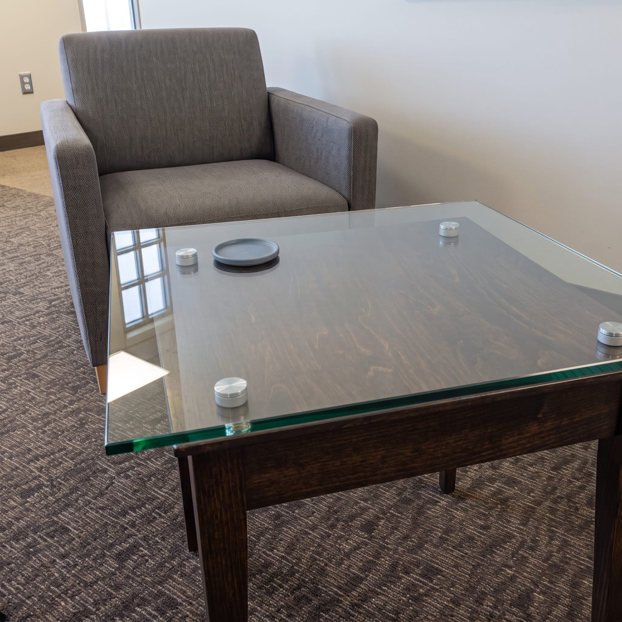 Rectangular clear glass protector mounted with metal standoffs on a dark wood coffee table.