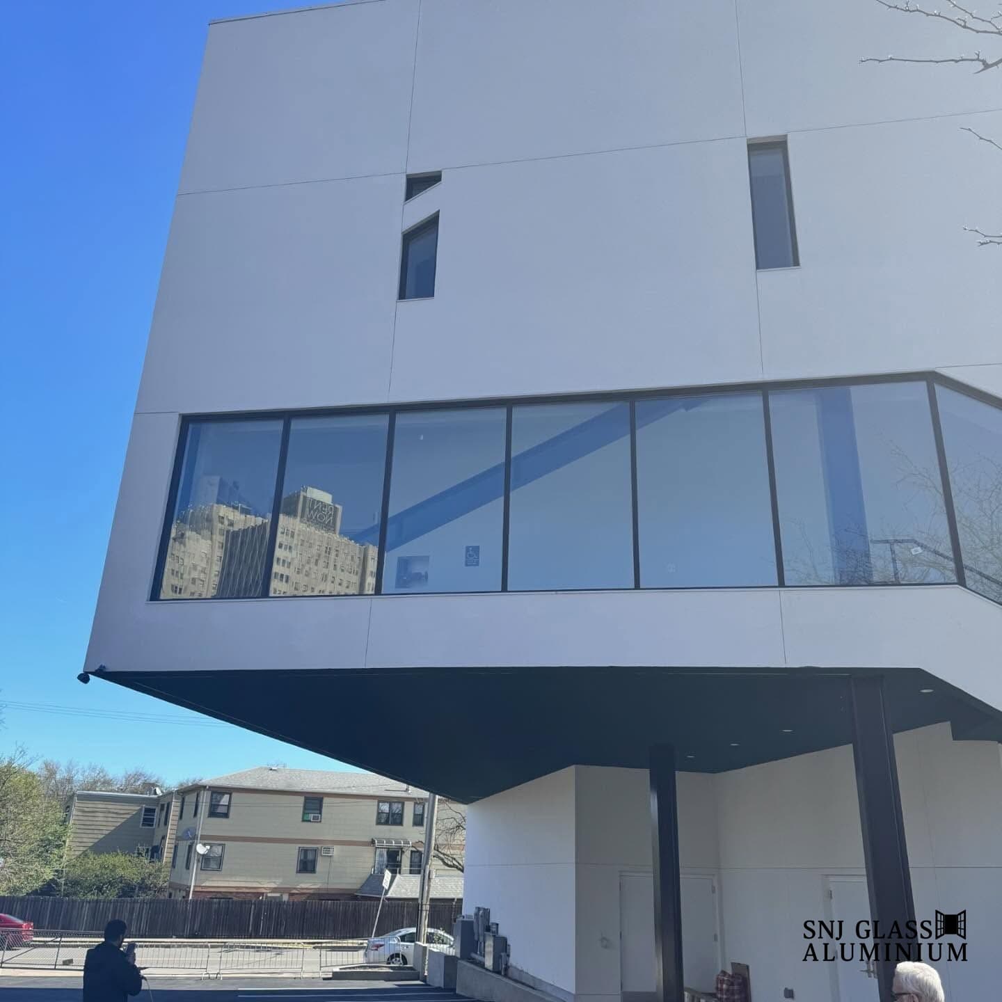 Large black-framed corner window wall installed across the upper floor of a modern white building.
