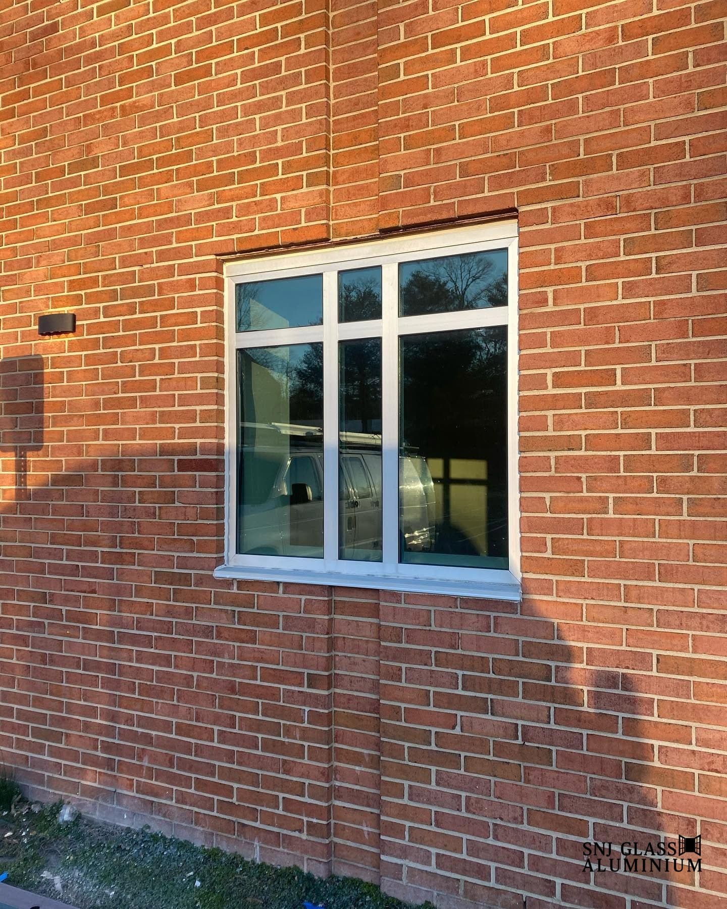 White-framed multi-panel window installed in a red brick exterior wall.