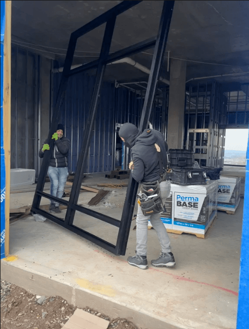 Installers positioning a large black storefront frame in Cliffside Park.